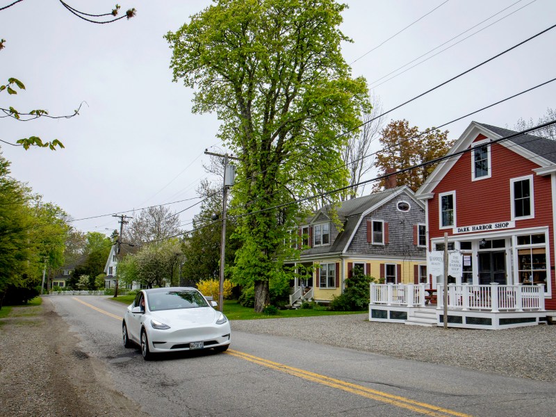 A Tesla drives on a road through a small town in Maine.